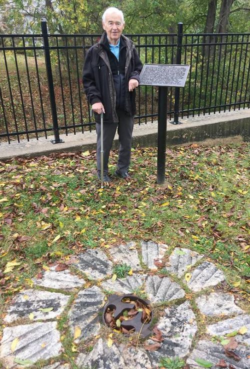 Dr Turner is pictured in the park next the dam, beside a millstone grain-grinding wheel which he donated to South Frontenac Township.